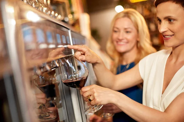 happy women pouring wine from dispenser at bar