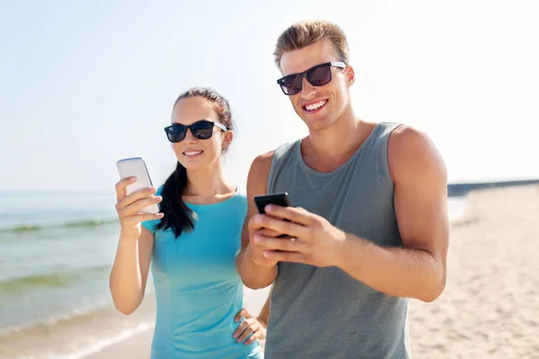 Paar in Sportkleidung mit Smartphones am Strand — Stockfoto