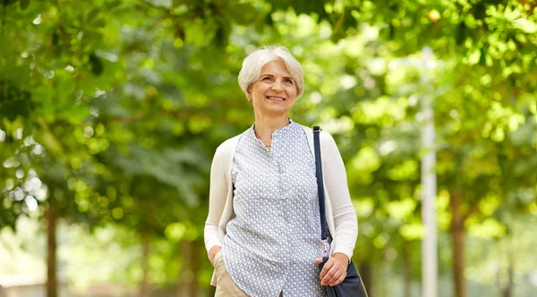 Счастливая пожилая женщина с сумочкой в летнем парке — стоковое фото