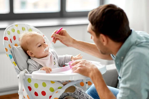 father feeding baby in highchair at home