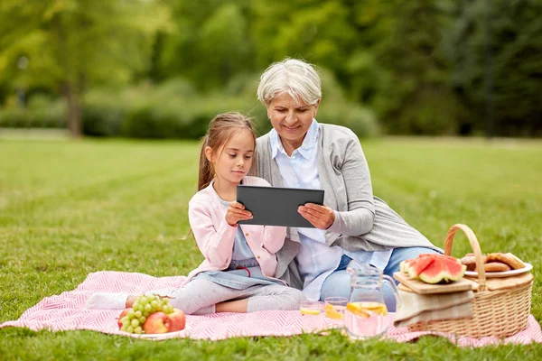 Grand-mère et petite-fille avec tablette au parc Image En Vente
