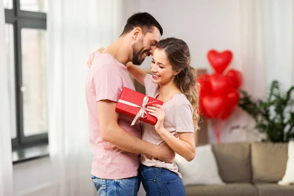 Glückliches Paar mit Geschenkbox, das sich zu Hause umarmt — Stockfoto
