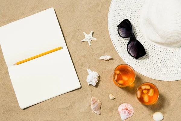 Notebook, cocktails, hat and shades on beach sand — Stock Photo, Image