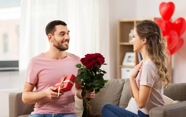 Lycklig man ger kvinna blommor och närvarande hemma — Stockfoto