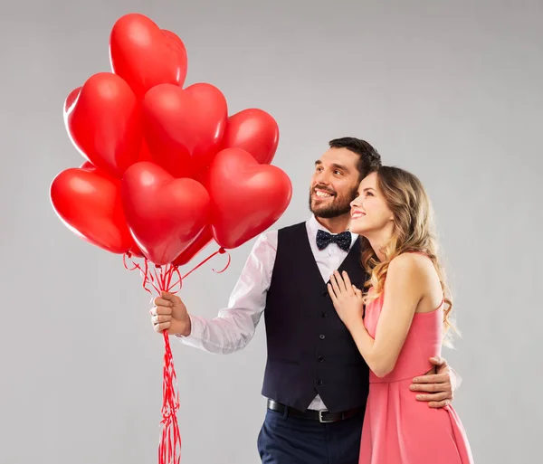 Feliz pareja con globos en forma de corazón rojo — Foto de Stock