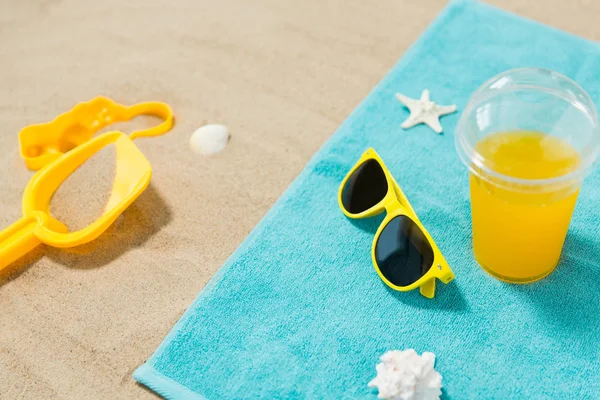 Occhiali da sole, giocattoli di sabbia e succo di frutta sul telo da spiaggia — Foto Stock