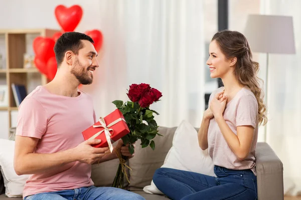 Счастливый мужчина дарит женщине цветы и подарок дома — стоковое фото