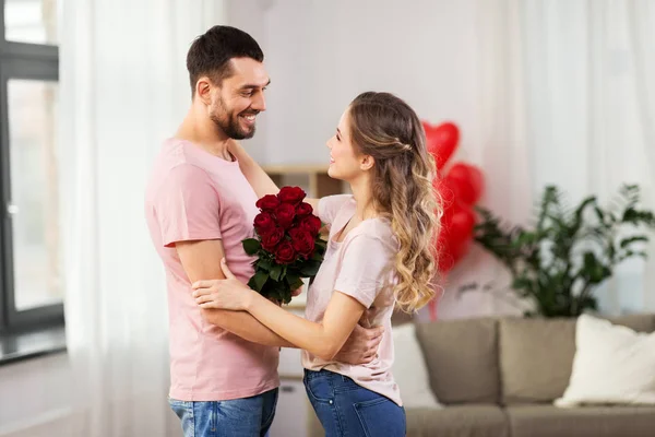 Happy couple with bunch of flowers hugging at home — Stock Photo, Image