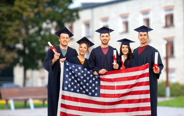 Estudiantes graduados con diplomas y bandera americana — Foto de Stock