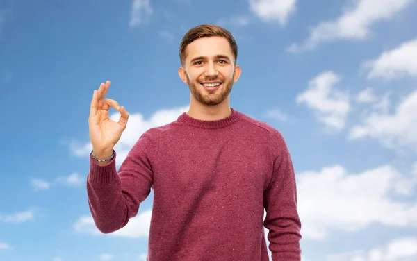 Usmívající se muž ukazuje značka ok ruky nad modrá obloha — Stock fotografie