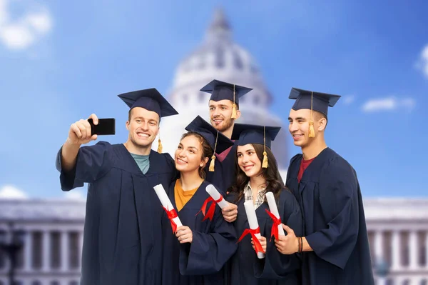 Graduates with diplomas taking selfie by cellphone — Stock Photo, Image