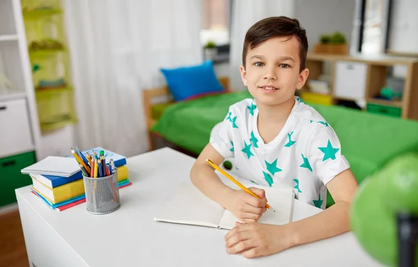 Glücklicher Junge schreibt oder zeichnet zu Hause an Notizbuch — Stockfoto