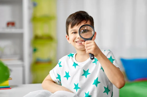 Niño feliz mirando a través de la lupa en casa — Foto de Stock