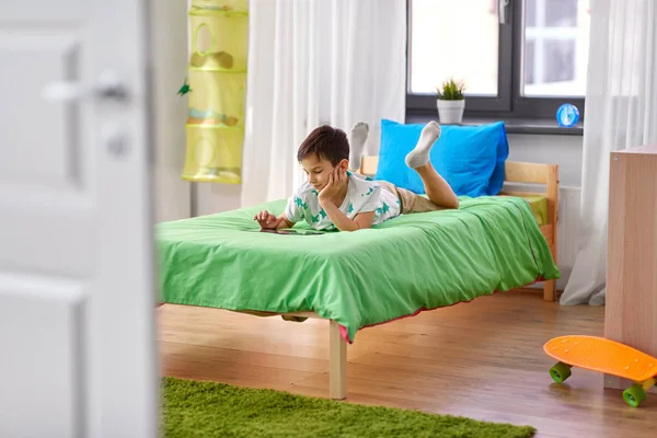 Chłopiec z komputera typu tablet pc, leżąc na łóżku w domu — Zdjęcie stockowe