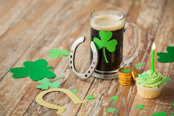 Glass of beer, horseshoe, green cupcake and coins — Stock Photo, Image