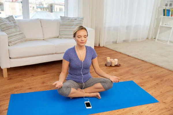 Mulher com música no smartphone meditando em casa — Fotografia de Stock