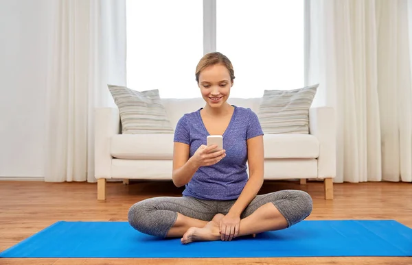 Vrouw met smartphone thuis yoga doen — Stockfoto