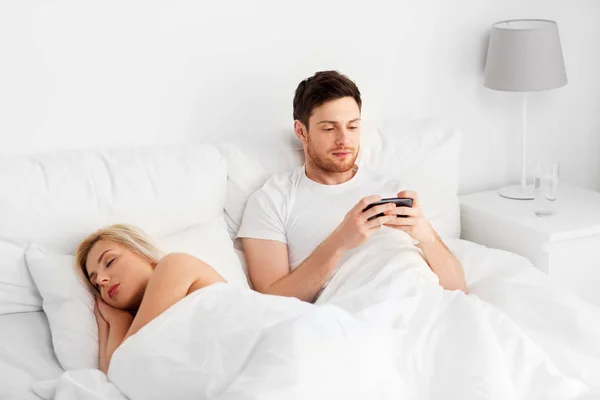 Kadın uyurken smartphone kullanan adam — Stok fotoğraf