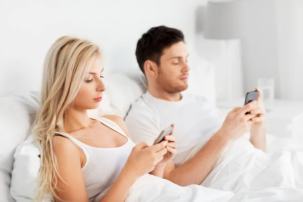 Pareja con smartphones en la cama — Foto de Stock