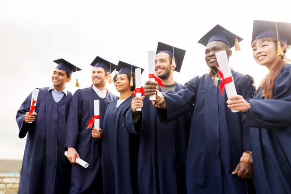 Gelukkige studenten in mortierplanken met diploma 's — Stockfoto