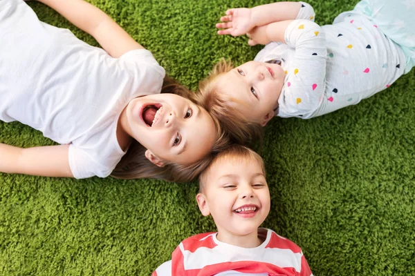 Niños pequeños y felices tumbados en el suelo o la alfombra —  Fotos de Stock