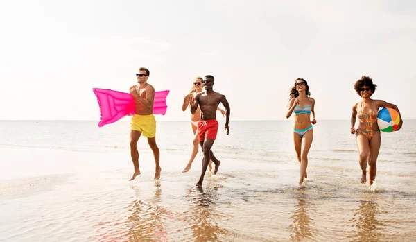 Amigos correr com bola de praia e colchão de natação — Fotografia de Stock