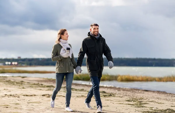 Casal com tumbler andando ao longo da praia de outono — Fotografia de Stock