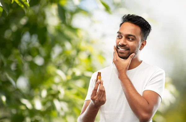 Uomo indiano sorridente che applica olio da toelettatura alla barba — Foto Stock