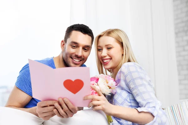Happy couple with greeting card and flowers — Stock Photo, Image