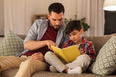 father and son reading book sofa at home clipart
