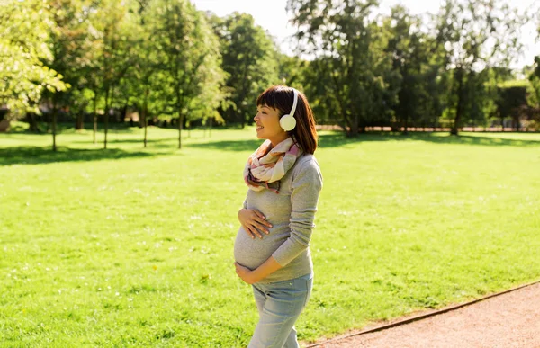 快乐怀孕的亚洲妇女在耳机在公园 — 图库照片