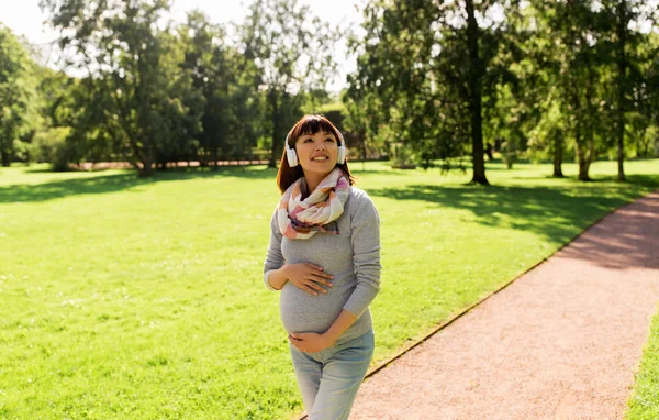 Happy pregnant asian woman in headphones at park — Stock Photo, Image
