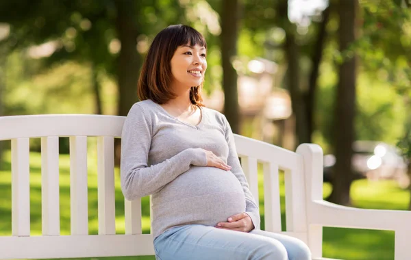 Gelukkig zwangere Aziatische vrouw zitten op bankje — Stockfoto