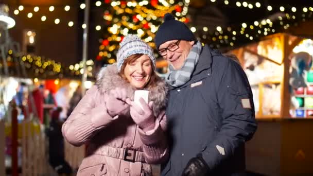 Pareja de ancianos con teléfono inteligente en el mercado de Navidad — Vídeos de Stock