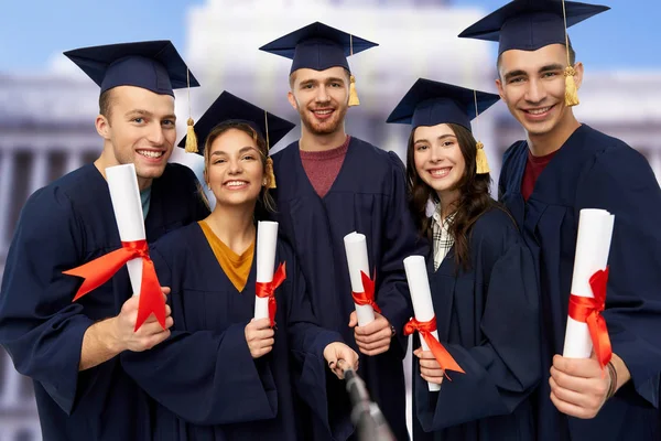 Happy graduates with diplomas taking selfie — Stock Photo, Image