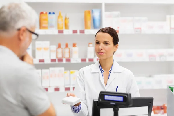 Аптекарь показывает препарат пожилому человеку в аптеке — стоковое фото
