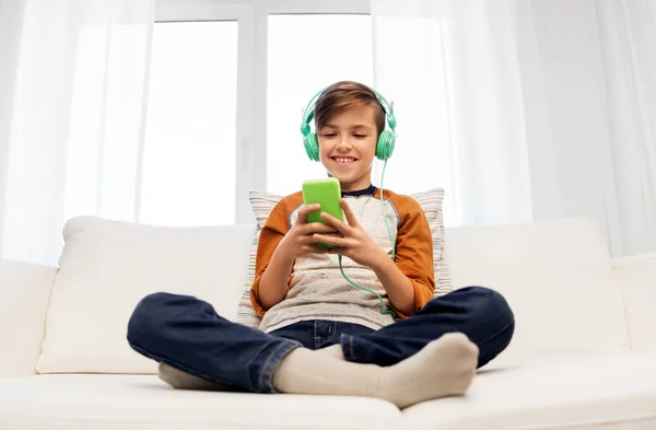 Niño feliz con teléfono inteligente y auriculares en casa —  Fotos de Stock