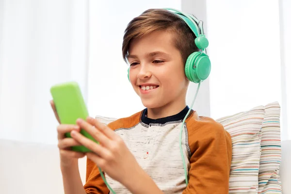Glad dreng med smartphone og hovedtelefoner derhjemme - Stock-foto