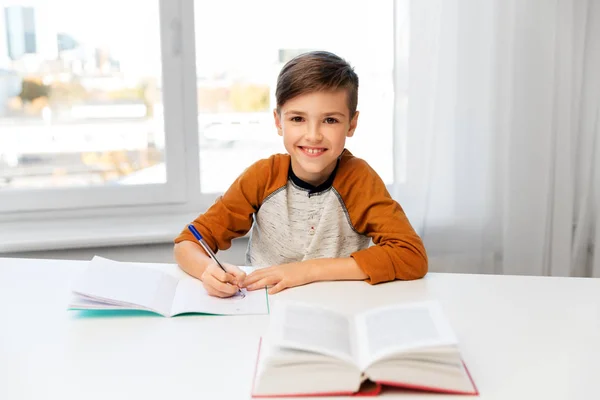 Fiú csinál házi feladatot, és írásban notebook otthon — Stock Fotó