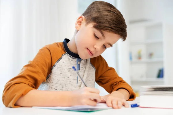 Menino fazendo lição de casa e escrevendo para notebook em casa — Fotografia de Stock