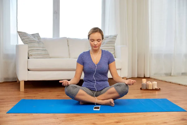 Mulher com música no smartphone meditando em casa — Fotografia de Stock