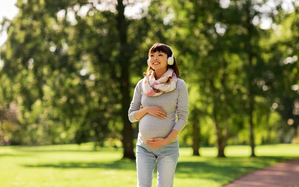 Feliz embarazada asiático mujer en auriculares en parque —  Fotos de Stock