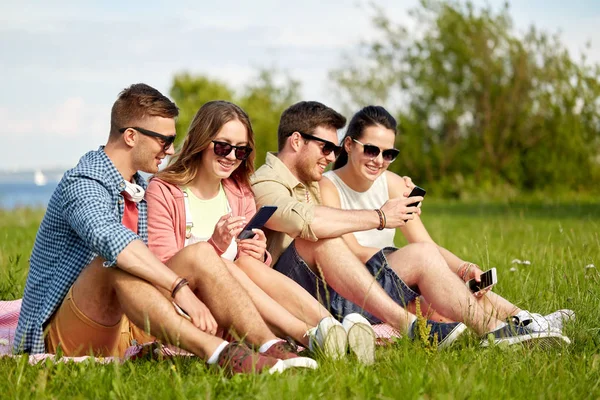 Lachende vrienden met smartphones zitten op gras — Stockfoto