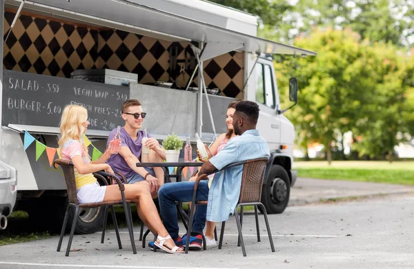 Friends with drinks sitting at table at food truck — Stock Photo, Image