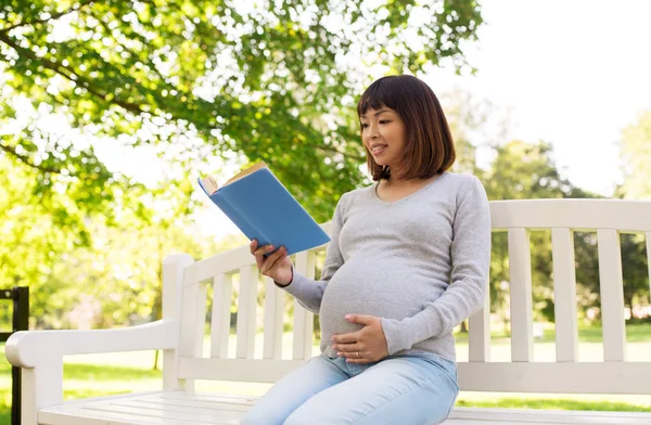 Happy pregnant asian woman reading book at park — Stock Photo, Image