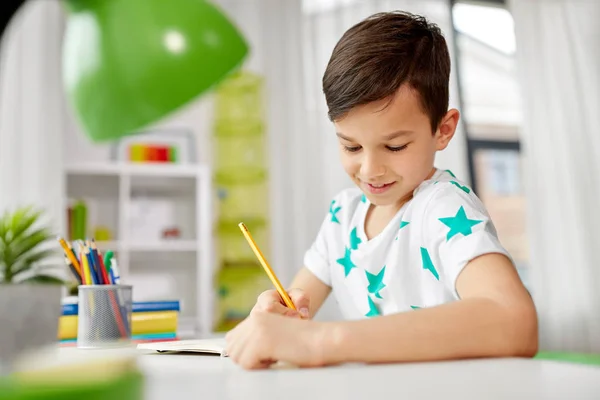 Счастливый мальчик пишет или рисует в тетрадь дома — стоковое фото
