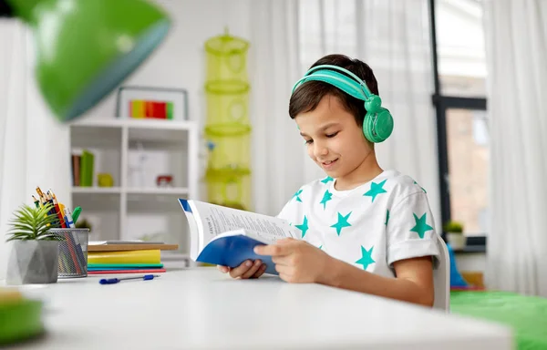 Ragazzo in cuffia con libro di testo imparare a casa — Foto Stock