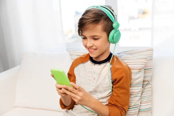 Niño feliz con teléfono inteligente y auriculares en casa —  Fotos de Stock