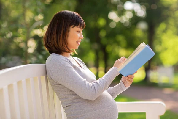 Heureux enceinte asiatique femme lecture livre à parc — Photo