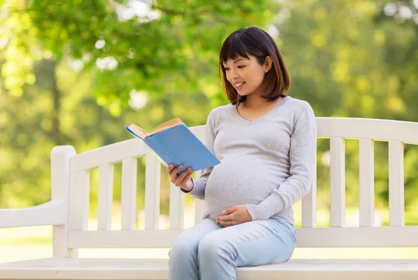 Heureux enceinte asiatique femme lecture livre à parc — Photo